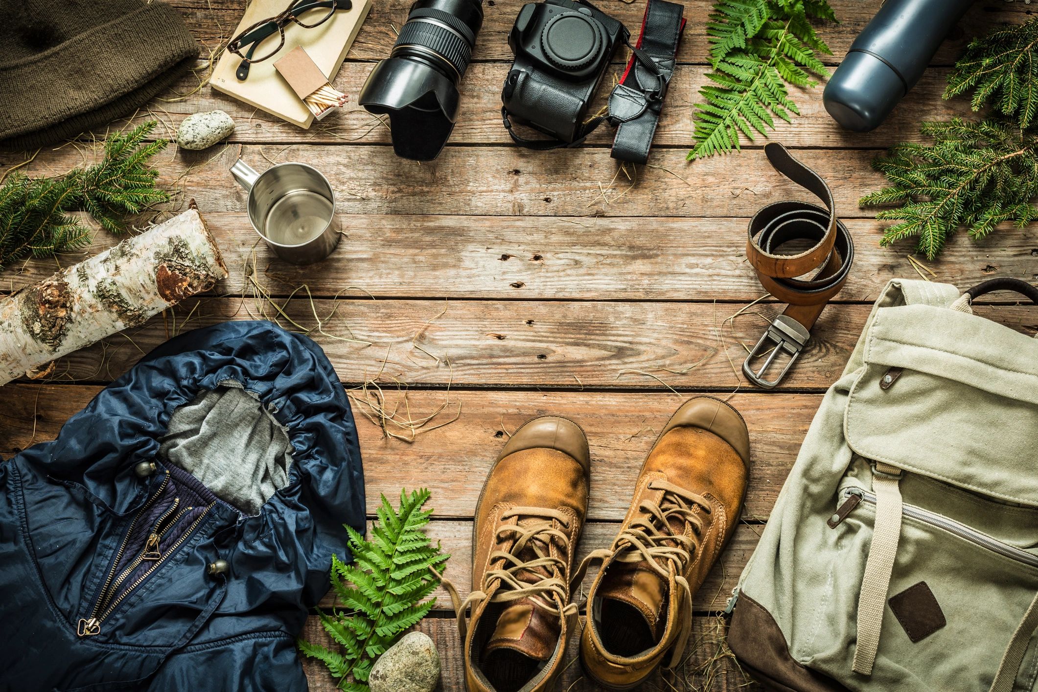 Backpack, jacket, boots, thermos, and camera arranged on wood