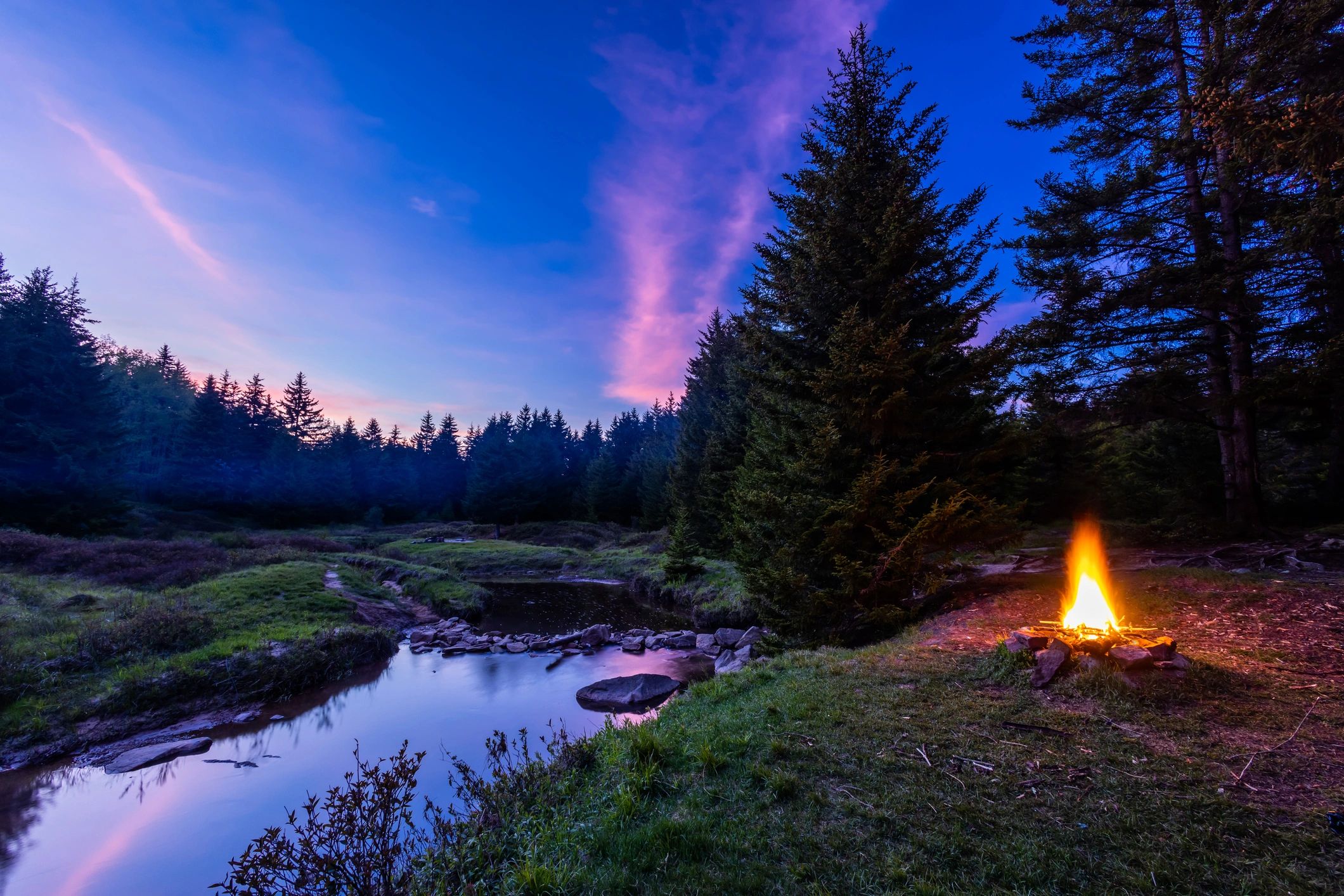 Campfire beside a creek at sunset in the wilderness